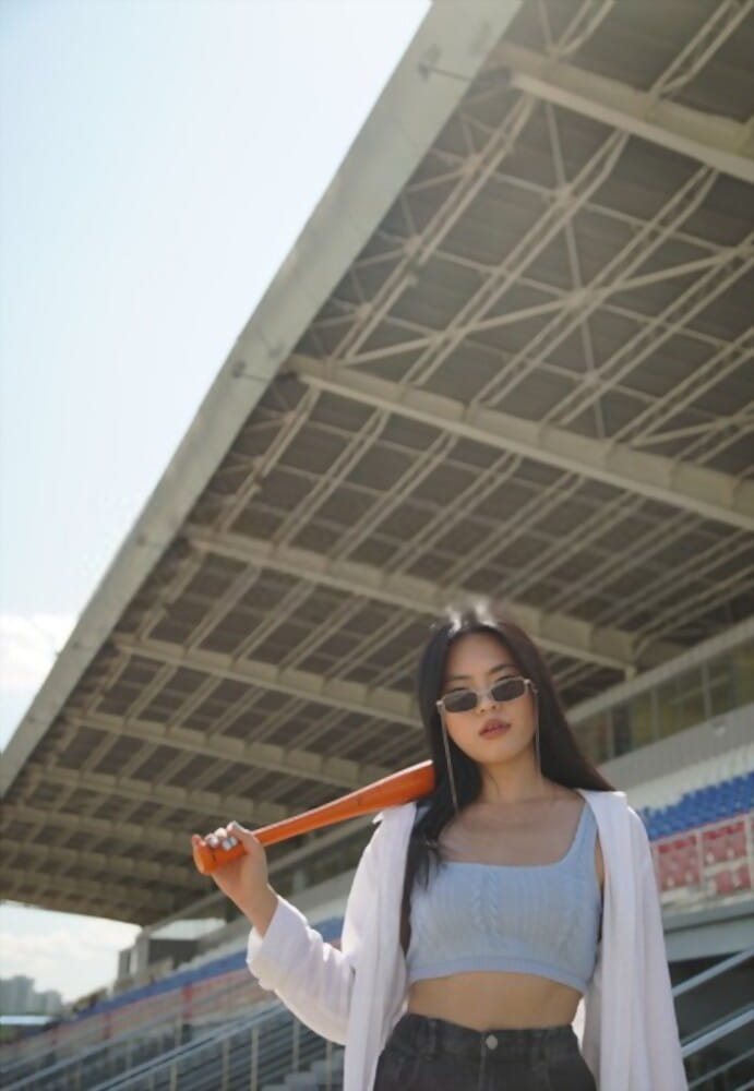 a girl with sunglasses, baseball bat, outfit in the baseball stadium