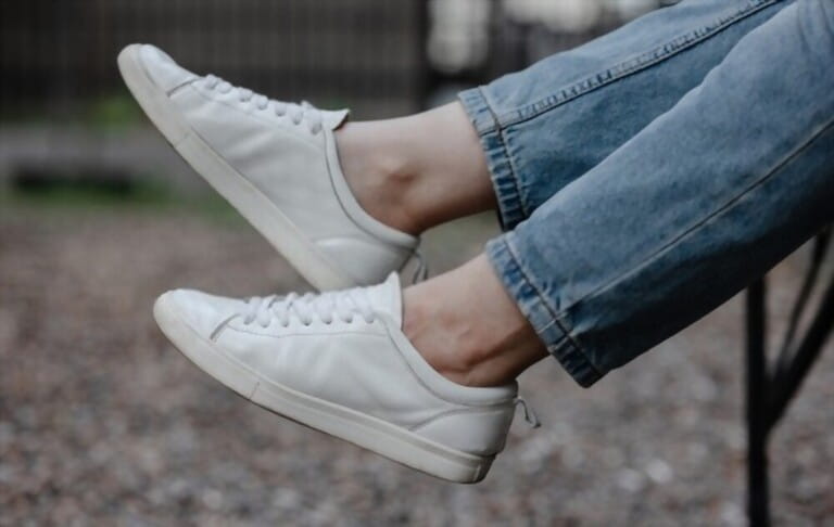 women's feet with white shoes and dark jeans