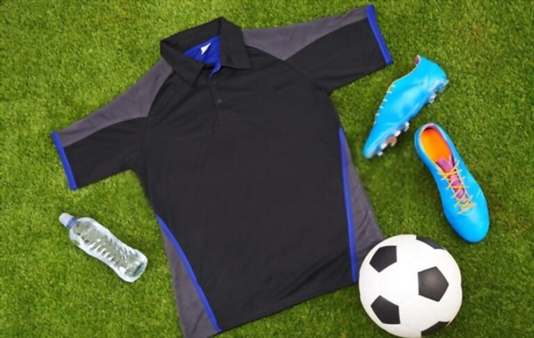Flatlay of sportswear or trendy soccer clothes, accessories and equipment on grass background. above view of modern sporty, active or fitness wear clothing style with water bottle, ball and trainers Flatlay of sportswear or trendy soccer clothes, accessories and equipment on grass background. above view of modern sporty, active or fitness wear clothing style with water bottle, ball and trainers