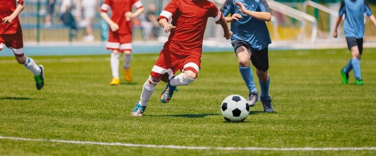 Football player running with the ball. Football player kicks soccer match. Young soccer player running after the ball. Children in red and blue football uniforms. Football Stadium
