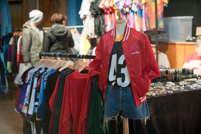 Bright red vintage American teen college jacket on a display at a vintage fair while a student couple browses a rail of clothes Bright red vintage American teen college jacket on a display at a vintage fair while a student couple browses a rail of clothes