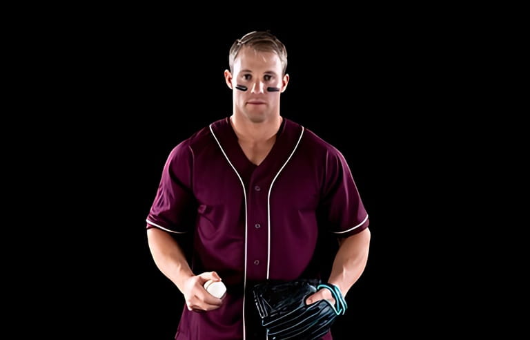Portrait of a Caucasian male baseball player, a pitcher or fielder, wearing a team uniform and a mitt, holding a baseball and looking to camera, with stripes of eye black under his eyes