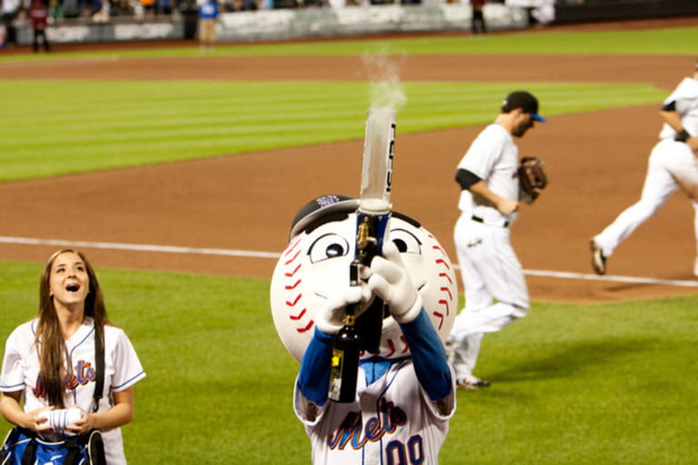 Mascot Mr. Mets at the MLB baseball game shooting a t-shirt gun with smoke at Citi Field Park stadium in New York.