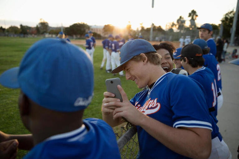 Playful baseball players with camera phone at fence Playful baseball players with camera phone at fence