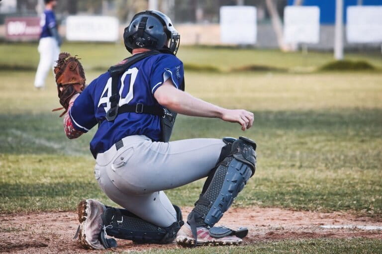 A baseball catcher raises a leather glove over one knee on the field